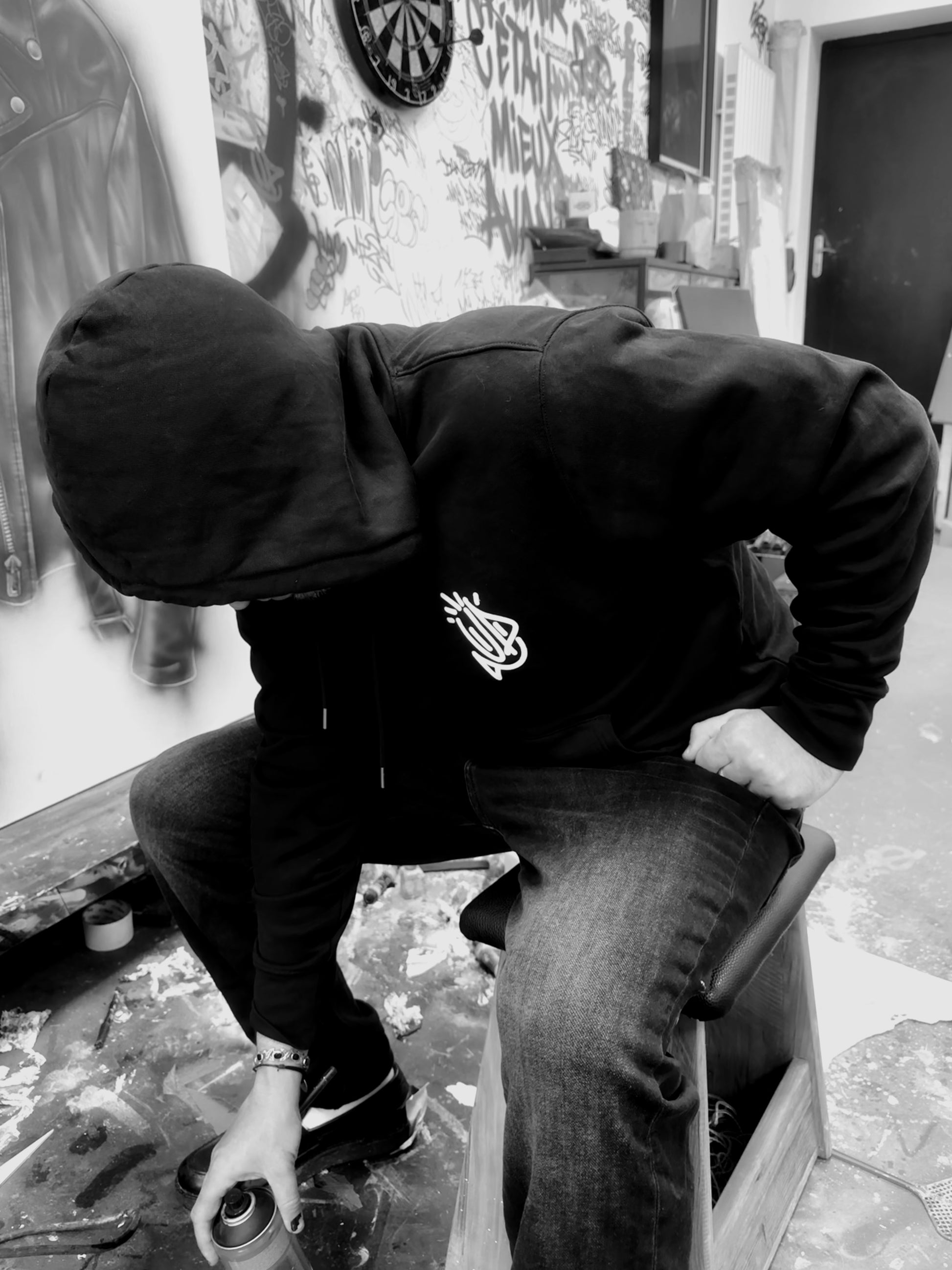 Artiste Onemizer en plein travail de création dans son atelier, portant le hoodie noir 4U de face devant une toile de street art 